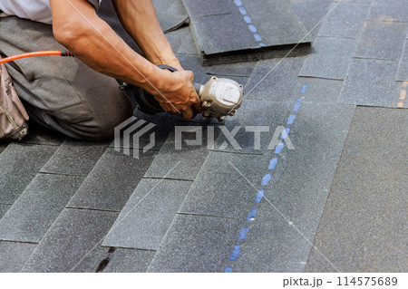New asphalt bitumen shingles are being installed by roofer using pneumatic air nail gun New asphalt bitumen shingles are being installed by roofer using pneumatic air nail gun 114575689