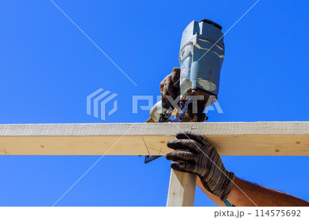 Framer uses an air nail hammer to install beams in wooden frame Framer uses an air nail hammer to install beams in wooden frame 114575692
