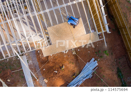 As construction worker hammers nails into OSB plywood panels on roof top As construction worker hammers nails into OSB plywood panels on roof top 114575694