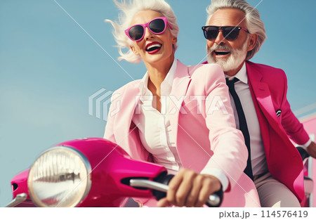 Cheerful happy senior couple riding pink scooter, stylish elderly woman and man drive moped in city 114576419