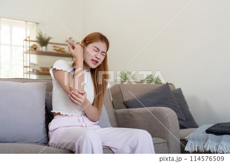 Young woman feeling pain in her elbow while sitting indoors Young woman feeling pain in her elbow while sitting indoors 114576509