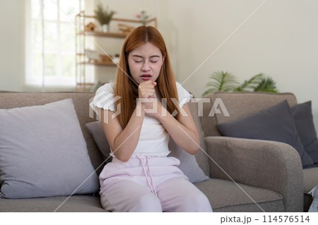 Young woman coughing while sitting on sofa at home Young woman coughing while sitting on sofa at home 114576514