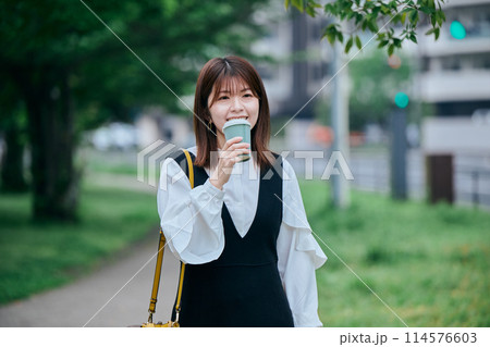 コーヒーカップを持ちながら歩く若い女性 コーヒーカップを持ちながら歩く若い女性 114576603