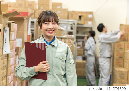 倉庫でバインダーを持つ作業着姿の若い女性 倉庫でバインダーを持つ作業着姿の若い女性 114576890