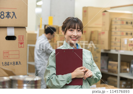 倉庫でバインダーを持つ作業着姿の若い女性 倉庫でバインダーを持つ作業着姿の若い女性 114576893