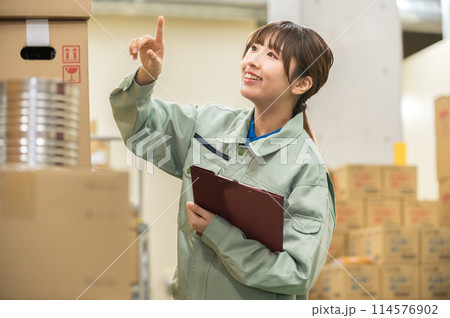 倉庫で検品作業する作業着姿の若い女性 倉庫で検品作業する作業着姿の若い女性 114576902