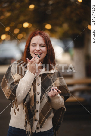 A cheerful redhead beams with joy on the streets of the autumn city. A cheerful redhead beams with joy on the streets of the autumn city. 114577153