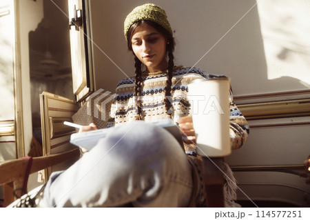 A fashionable lady embraces her hippie persona against the natural beauty of the park, with a trailer nearby. 114577251