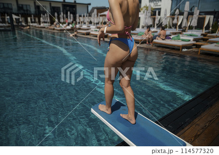 A radiant girl in a blue bikini poses against the vivid blue pool water. 114577320