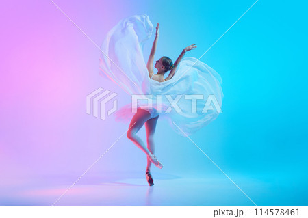 Portrait of young ballerina dancing standing on tiptoe with fabric in neon light against vivid gradient background. 114578461