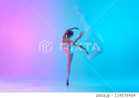 Graceful ballet artist performing with white fabric in action in neon light against vivid gradient background. Art. Graceful ballet artist performing with white fabric in action in neon light against vivid gradient background. Art. 114578484