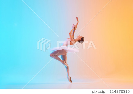 Young ballerina in white tutu dancing and leaning backwards in motion in neon light against blue-orange gradient background. Young ballerina in white tutu dancing and leaning backwards in motion in neon light against blue-orange gradient background. 114578510