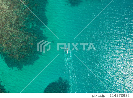 Aerial top view of Banca boat floating in open sea with clear and turquoise water on sunny day . Tropical landscape. Philippines, Palawan. 114578982