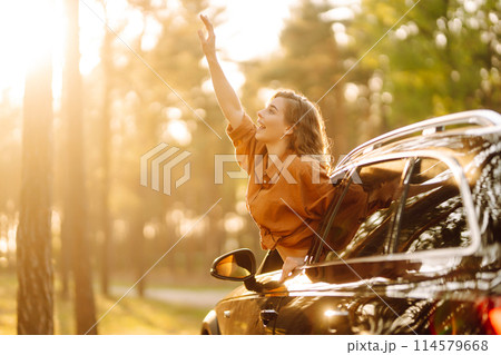 Beautiful traveler woman is resting and enjoying the sunset in the car. Active lifestyle, tourism. 114579668