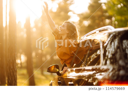 Beautiful traveler woman is resting and enjoying the sunset in the car. Active lifestyle, tourism. 114579669