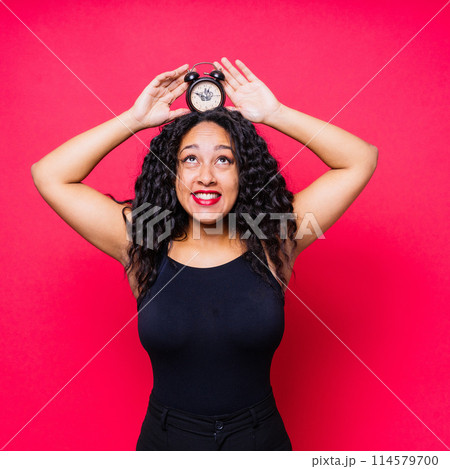 Smiling young african american woman posing isolated on red background with clock Smiling young african american woman posing isolated on red background with clock 114579700
