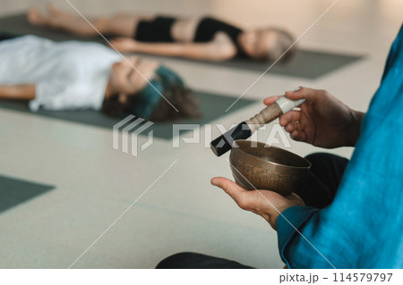Children relax lying down to the sounds of a Tibetan bowl in the fitness room. Children's yoga 114579797