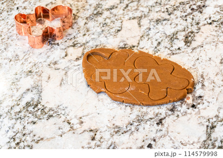 In a contemporary white kitchen, gingerbread cookie dough is skillfully rolled out, setting the stage for a delightful holiday treat. In a contemporary white kitchen, gingerbread cookie dough is skillfully rolled out, setting the stage for a delightful holiday treat. 114579998