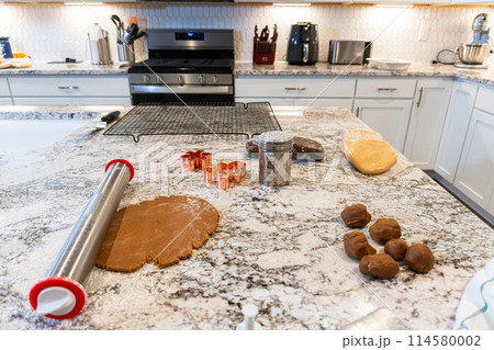 In a contemporary white kitchen, gingerbread cookie dough is skillfully rolled out, setting the stage for a delightful holiday treat. 114580002