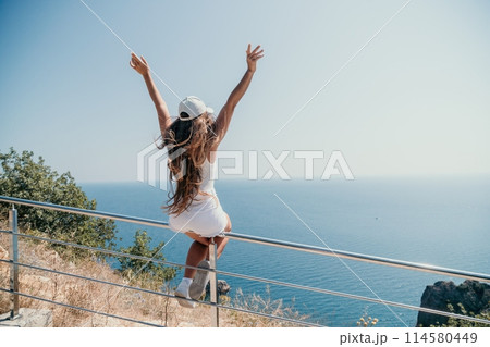 Woman summer travel sea. Happy tourist enjoy taking picture outdoors for memories. Woman traveler posing over sea bay surrounded by volcanic mountains, sharing travel adventure journey 114580449