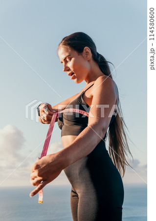 A woman is holding a pink tape measure and is measuring her breasts after morning fitness 114580600