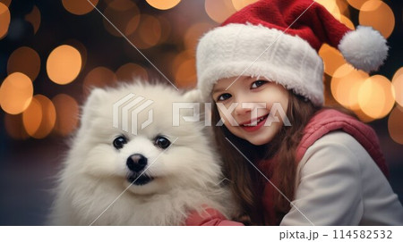 Smiling cute 7 years old girl in Santa hat hugs a white small dog on golden bokeh background, selective focus. 114582532