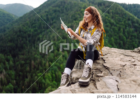 Traveler with yellow backpack and map in hands on a cliff in the mountains. Adventure concept. Traveler with yellow backpack and map in hands on a cliff in the mountains. Adventure concept. 114583144