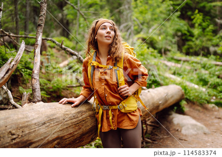 Smiling woman traveler along a forest hiking trail in the mountains against the backdrop of nature. Smiling woman traveler along a forest hiking trail in the mountains against the backdrop of nature. 114583374