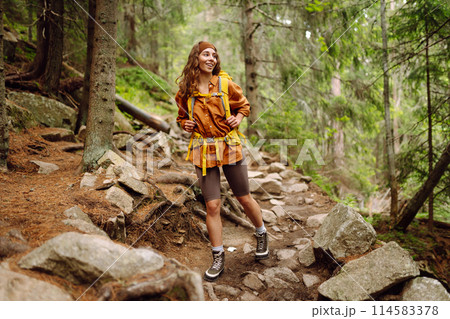 Smiling woman traveler along a forest hiking trail in the mountains against the backdrop of nature. Smiling woman traveler along a forest hiking trail in the mountains against the backdrop of nature. 114583378
