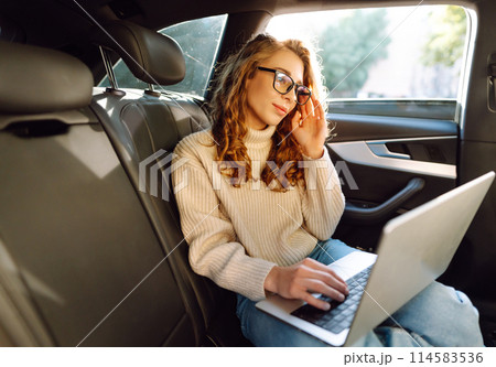 Business transportation. Woman with laptop works in back seat of car. Concept of transport. Business transportation. Woman with laptop works in back seat of car. Concept of transport. 114583536