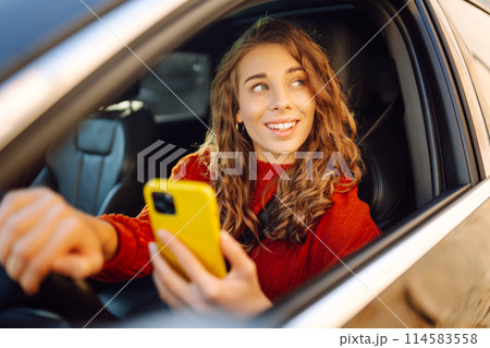 Portrait of a young woman sitting in a car in the driver's seat looking into a smartphone. Portrait of a young woman sitting in a car in the driver's seat looking into a smartphone. 114583558