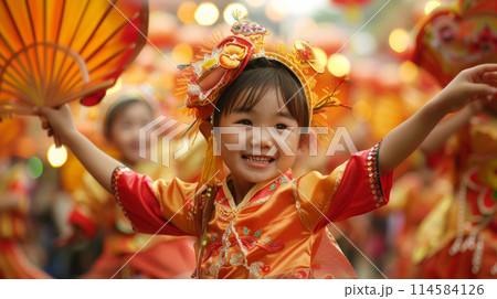 Asian child in colorful traditional outfit celebrating at a vibrant festival with others, smiling. 114584126