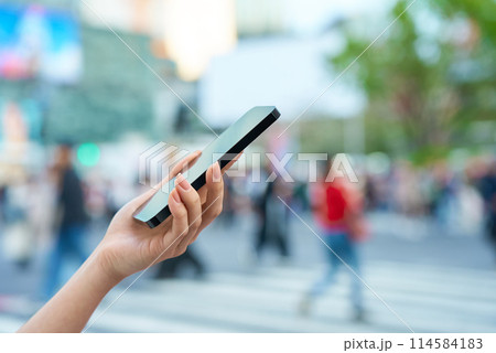 繁華街でスマートフォンを操作する女性の手元 114584183