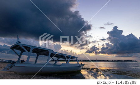 A boat rests on the sandy beach as the sunset over the horizon 114585289