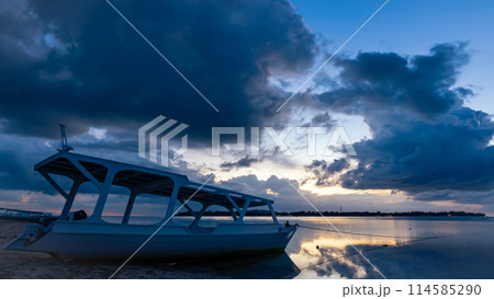 A boat rests on the sandy beach as the sunset over the horizon 114585290