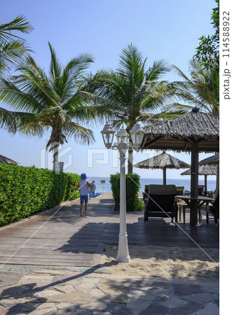 The boy runs to the beach to the sea along a wooden path past a lantern and palm trees 114588922