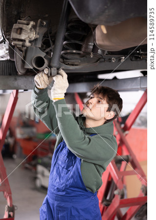 Young mechanic repairing undercarriage of vehicle on lift in auto repair workshop Young mechanic repairing undercarriage of vehicle on lift in auto repair workshop 114589735