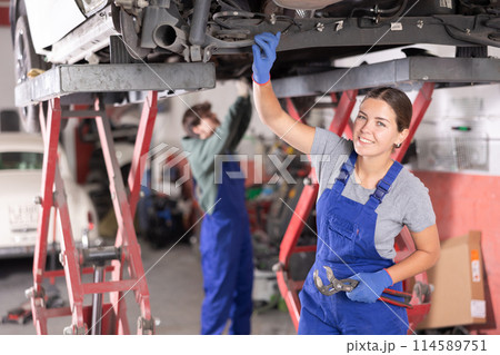 Female mechanic checking the rear suspension shock absorber of car 114589751