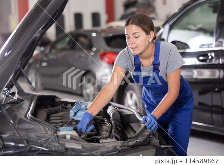Young female mechanic repairs under hood of car Young female mechanic repairs under hood of car 114589867