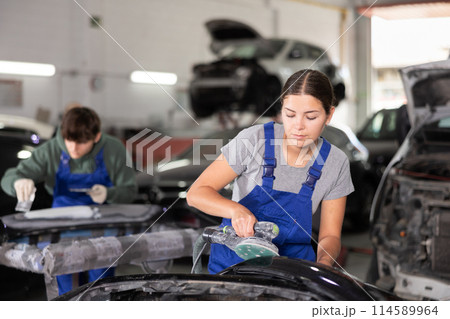 Woman auto mechanic using grinding machine prepares car parts for painting 114589964