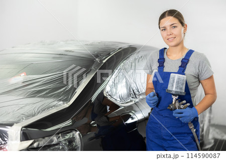 Young woman mechanic paints car with machine 114590087
