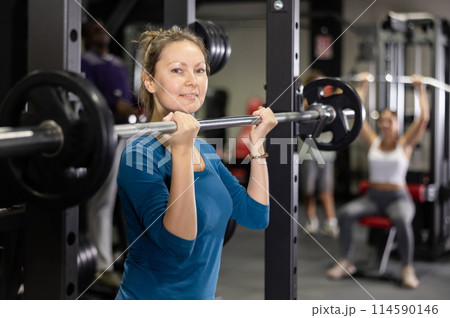 Caucasian woman doing exercises usining barbell and half rack in gym 114590146