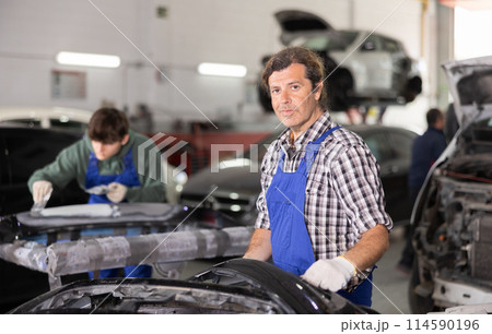 Middle-aged auto repair workshop owner standing among repaired cars Middle-aged auto repair workshop owner standing among repaired cars 114590196