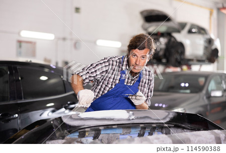 Man prepares car for painting in workshop - grinds and puts putty on bumper before painting 114590388