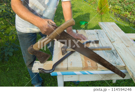man uses a hacksaw, a hatchet, a claw hammer for construction work in your garden man uses a hacksaw, a hatchet, a claw hammer for construction work in your garden 114594246