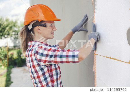 Insulation of the house with polyfoam. The worker is checking with the construction level the accuracy of the installation of polystyrene board on the facade. 114595762