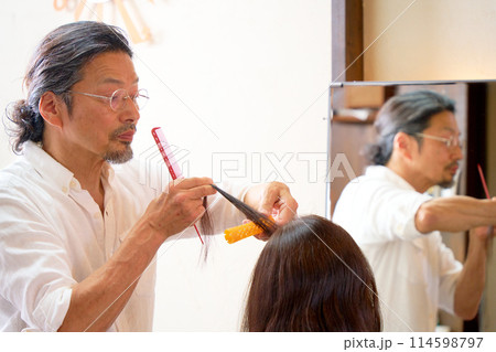 ヘアサロンにてワインディングを行うベテランの男性美容師 ヘアサロンにてワインディングを行うベテランの男性美容師 114598797
