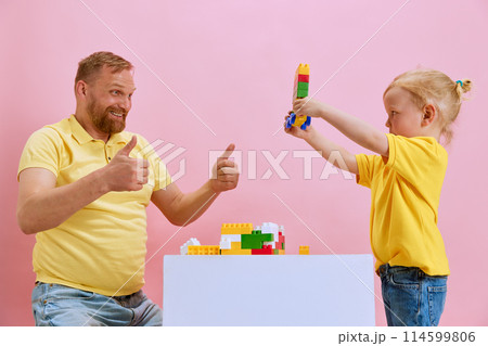 Little son showing with his father his little building while they playing against pink studio background. Man showing thumb up. Little son showing with his father his little building while they playing against pink studio background. Man showing thumb up. 114599806