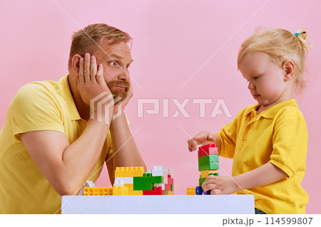 Cute moments. Father and his little son enjoying building block activity. against pink studio background. Family playtime. Cute moments. Father and his little son enjoying building block activity. against pink studio background. Family playtime. 114599807