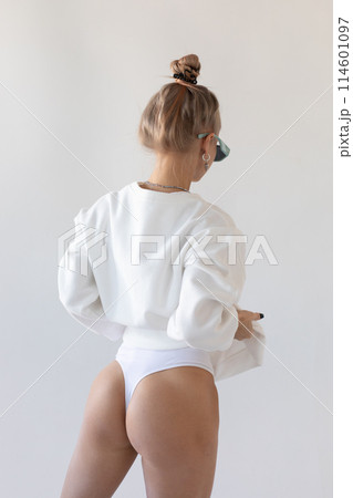 Beautiful blonde girl in a hoodie and panties posing with her back on a white background Beautiful blonde girl in a hoodie and panties posing with her back on a white background 114601097
